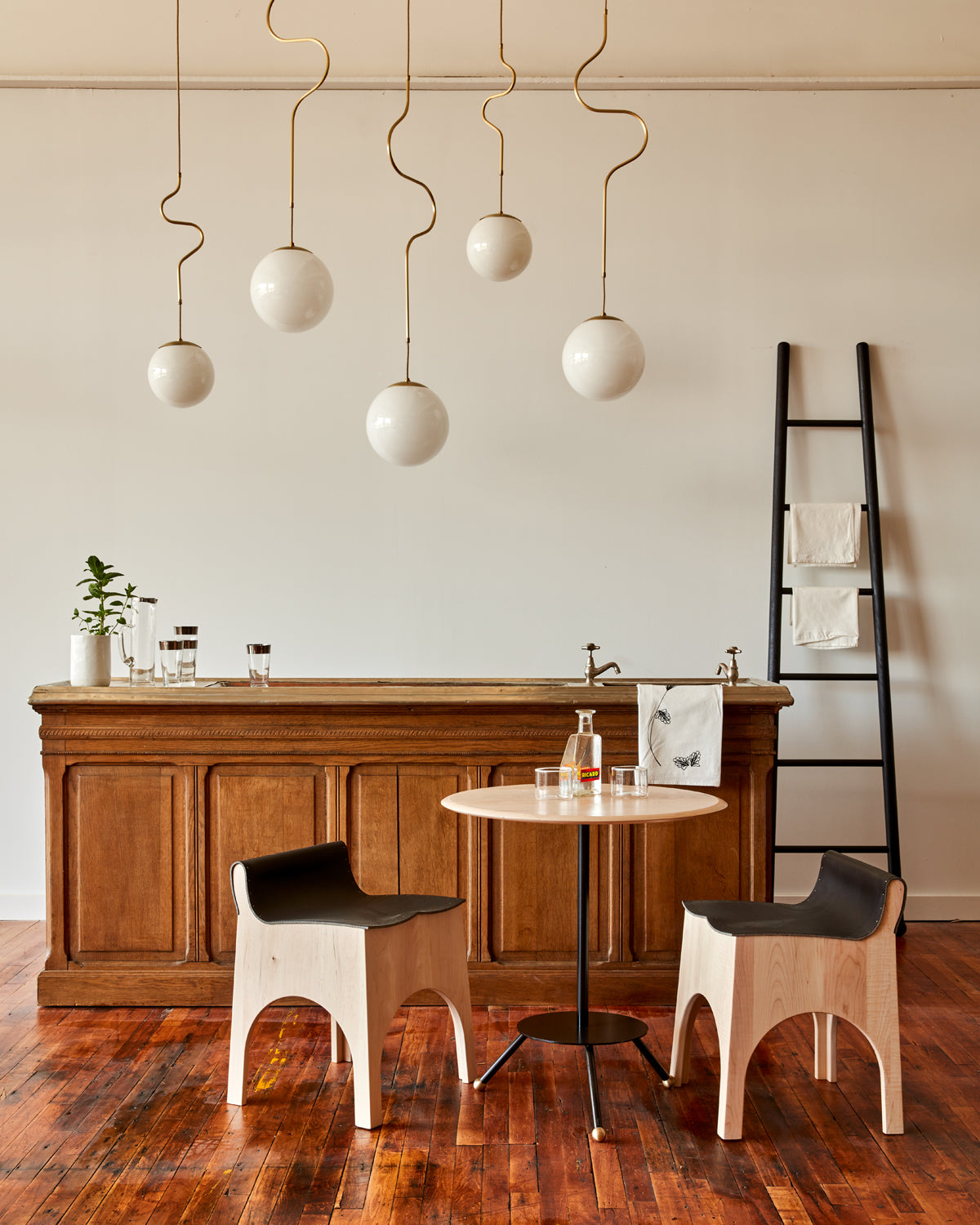 Modern brass globe pendant light with warm satin brass curved body and white milk glass globe over bar counter
