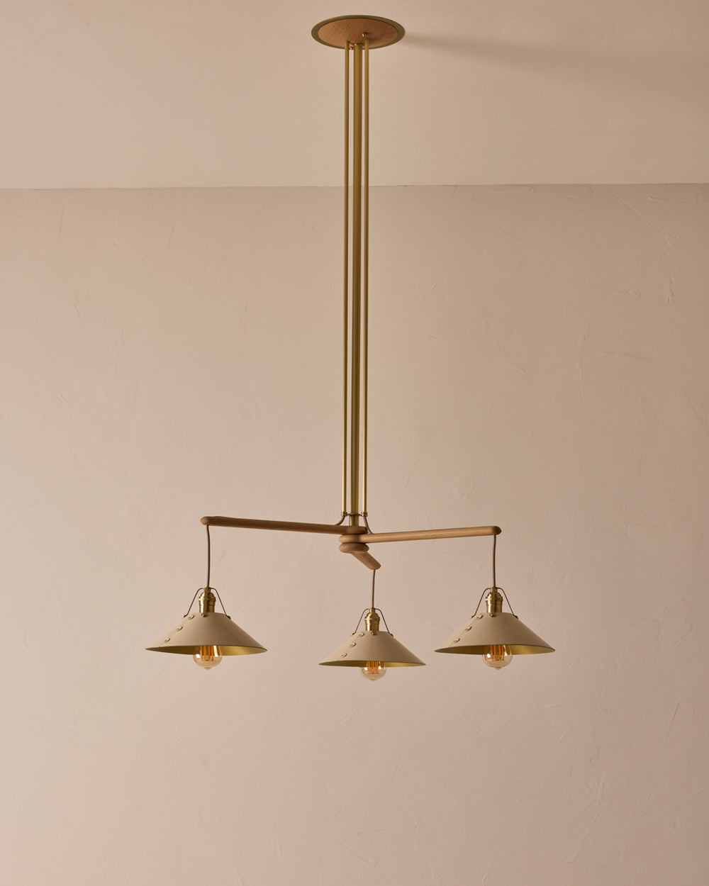 A three-arm chandelier with brass metal poles and white leather shades, suspended from a white oak canopy. #leather-shade_eggshell