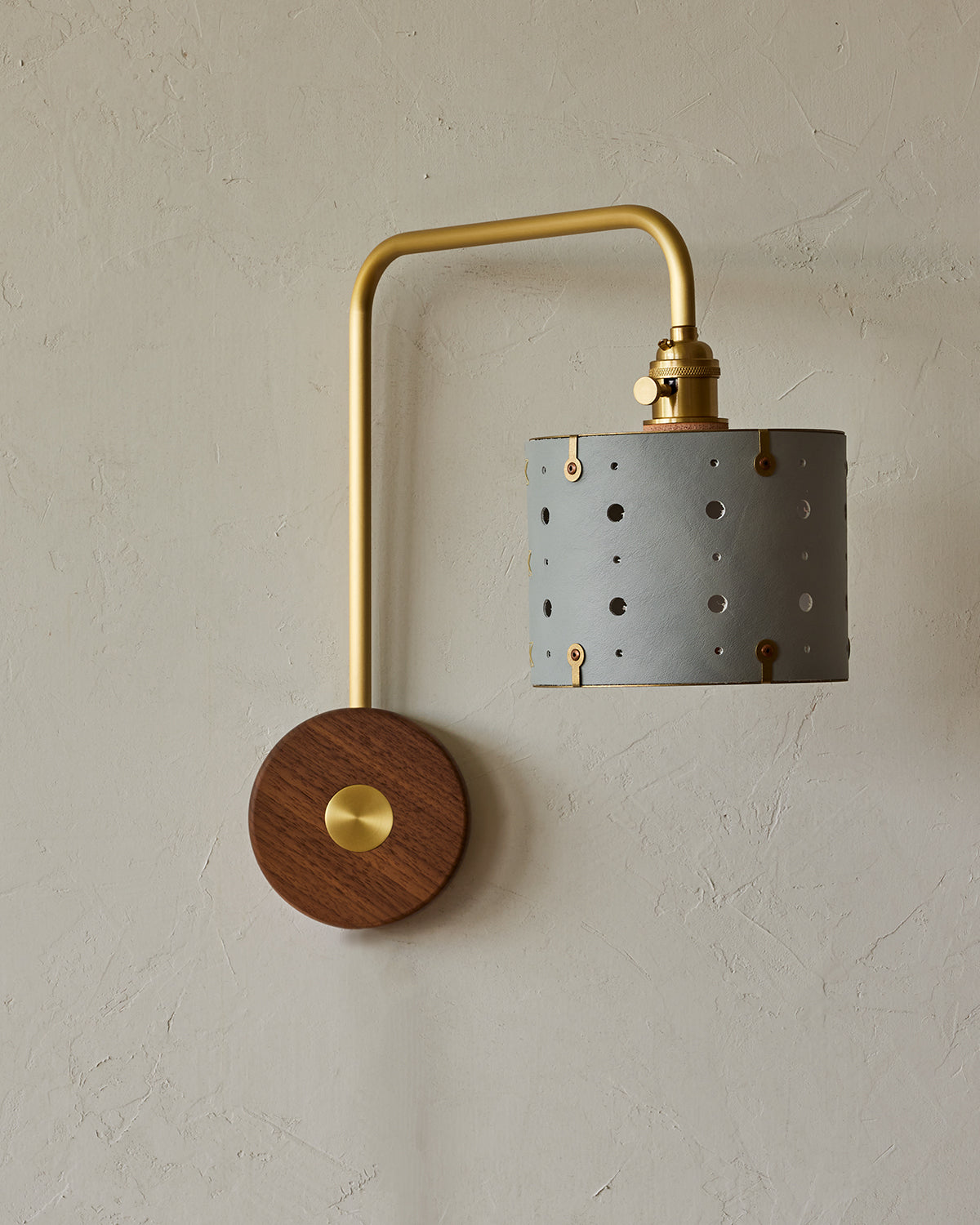 Articulating satin brass sconce with blue handstitched leather shade and walnut backplate