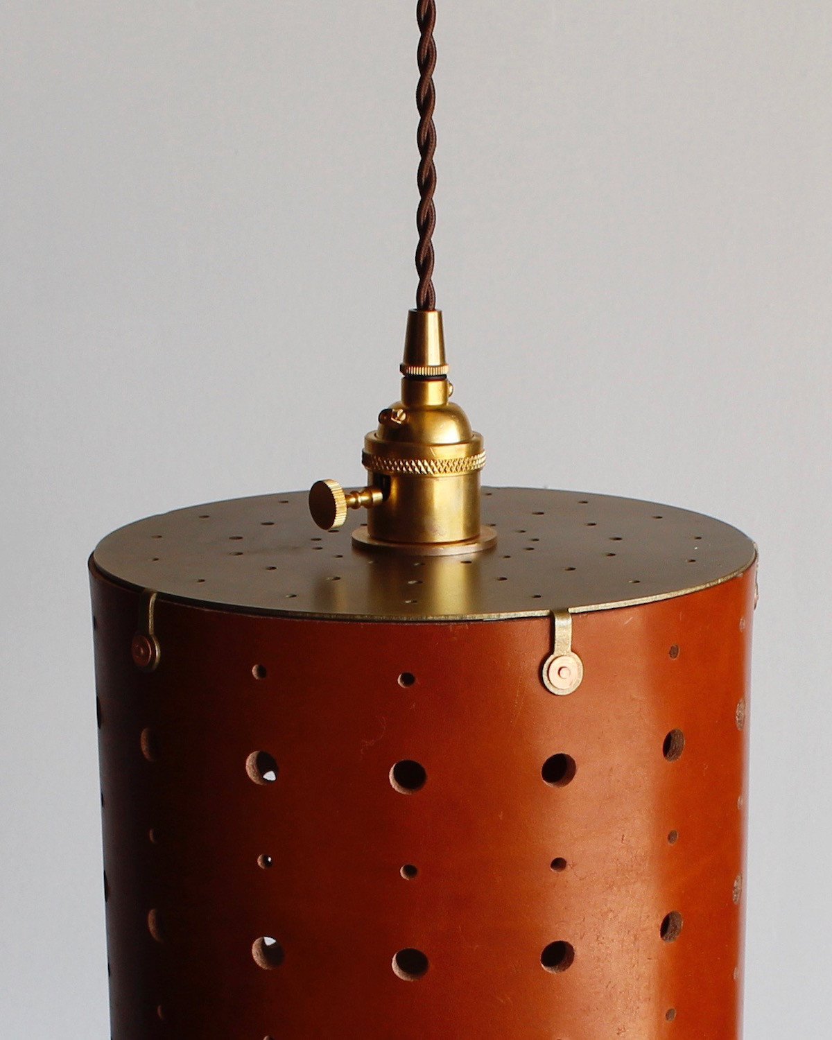 Tan leather cylinder pendant with handstitched, perforated leather shade. Made by Lostine in Philadelphia. Hardwired or plug light fixture. Simple interior design, made in the USA.