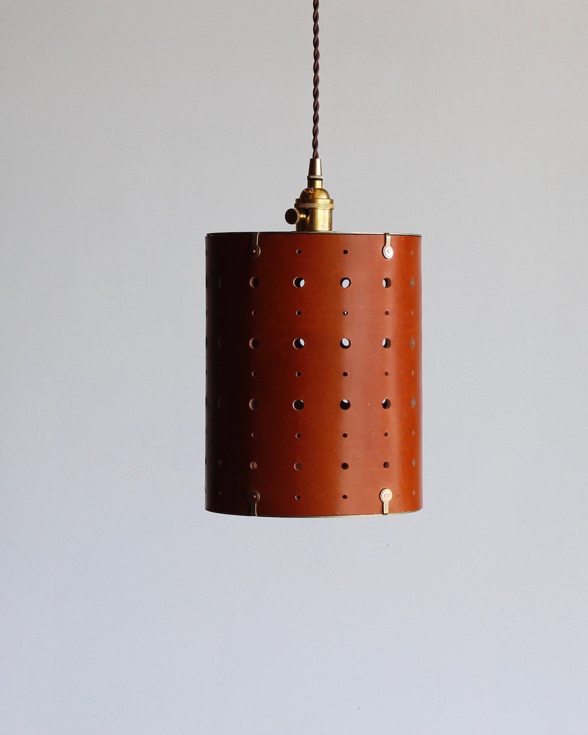 Tan leather cylinder pendant with handstitched, perforated leather shade. Made by Lostine in Philadelphia. Hardwired or plug light fixture. Simple interior design, made in the USA.