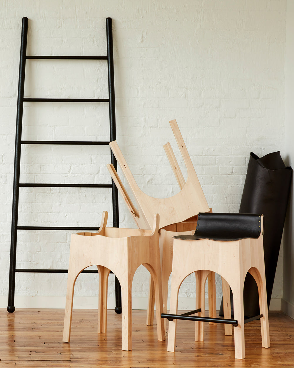 Sculpted stool with black leather and maple wooden base with metal foot rest and short backrest. Pictured with XL Wide Black Ladder. Counter and bar height. Handmade in Philadelphia by Lostine. Simple Interior Design. Warm American Modern Design #leather-finish_black harness