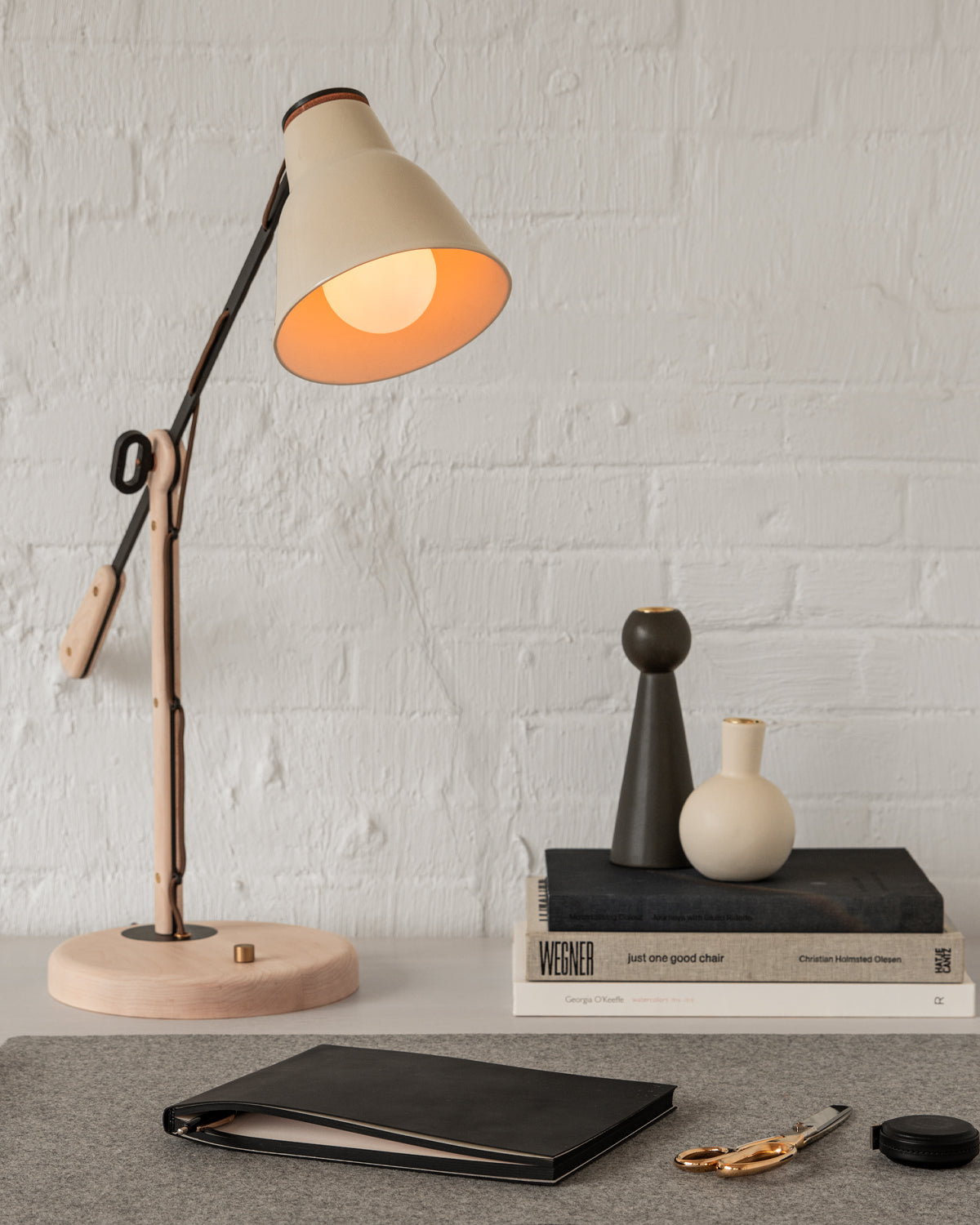 Side table lamp with articulating arm and ceramic shade on deskscape with office supplies, books and candle holders #color_cream