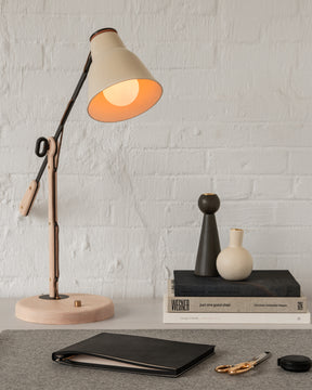 Side table lamp with articulating arm and ceramic shade on deskscape with office supplies, books and candle holders