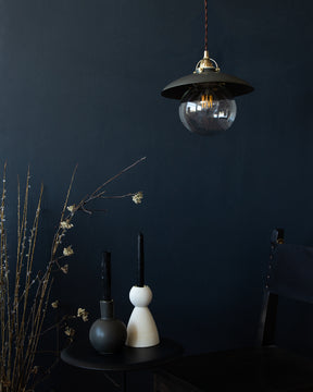 Matte black ceramic pendant light hanging above ebony side table with ceramic candle holders