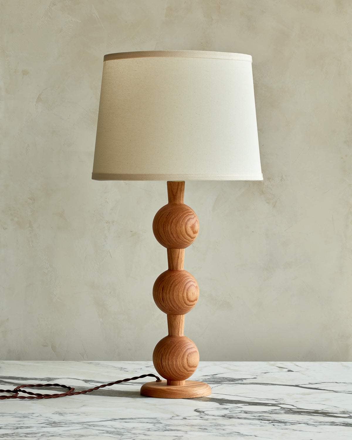 Sculptural solid wood table lamp with barbell design in natural finish with ivory linen shade