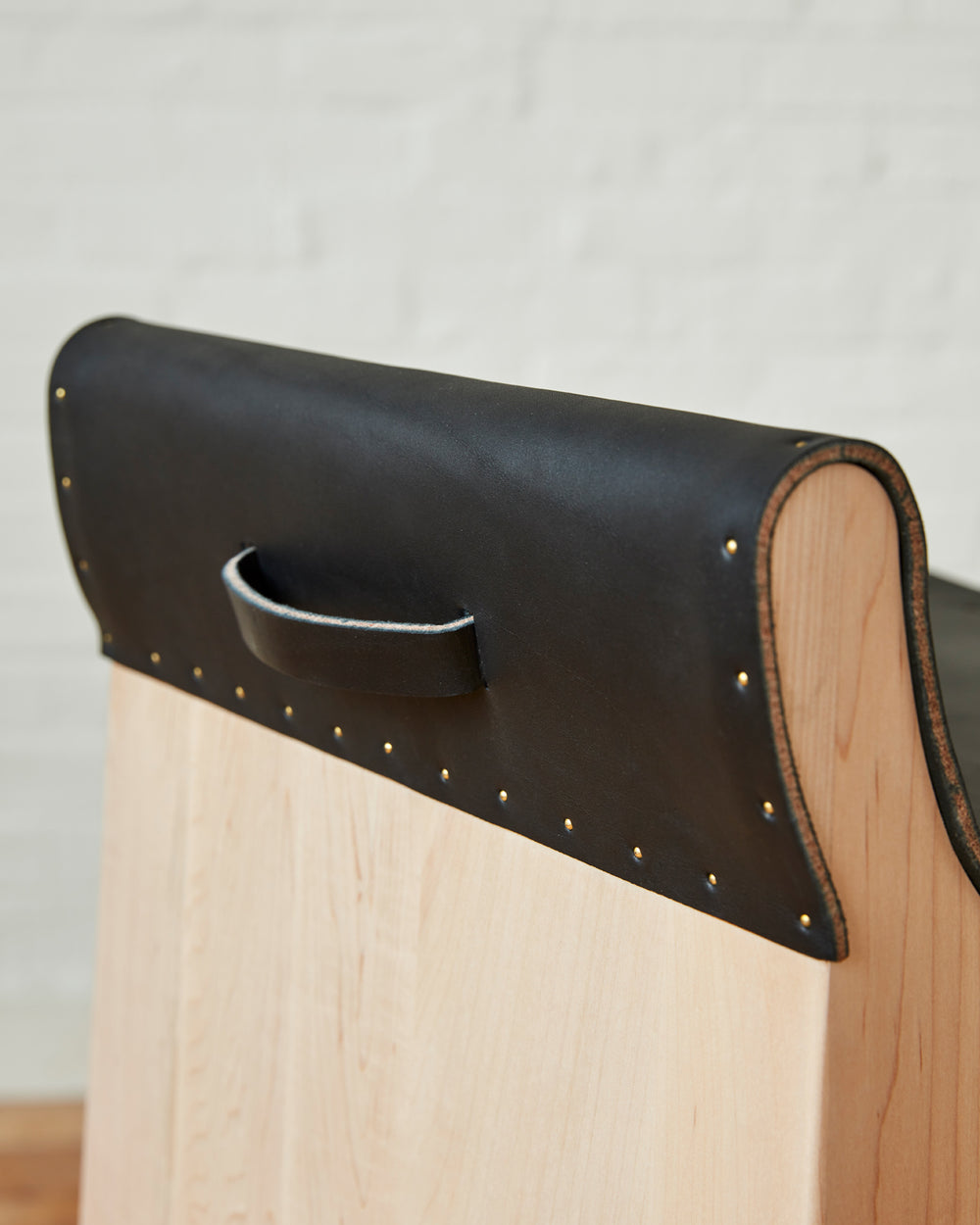 Leather pull handle of Sculpted stool with black leather and maple wooden base with metal foot rest and short backrest. Counter and bar height. Handmade in Philadelphia by Lostine. Simple Interior Design. Warm American Modern Design #leather-finish_black harness