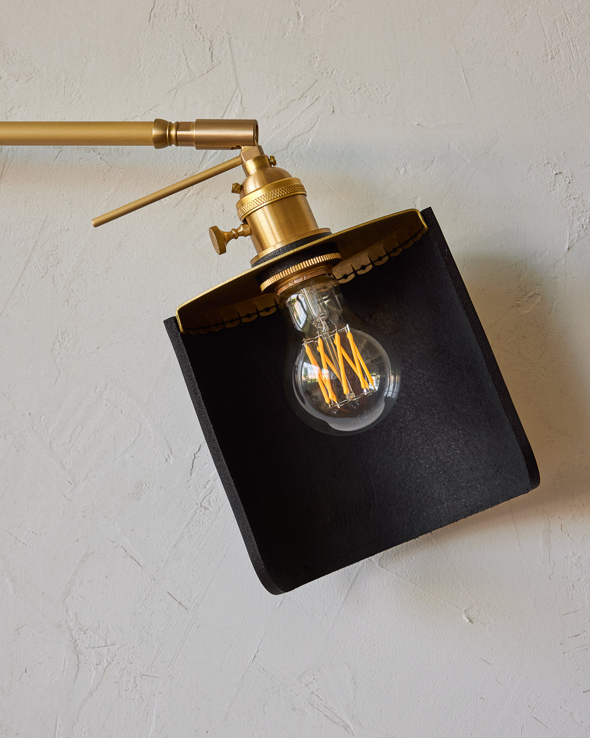 Curved black leather and brass shade for articulating wall sconce