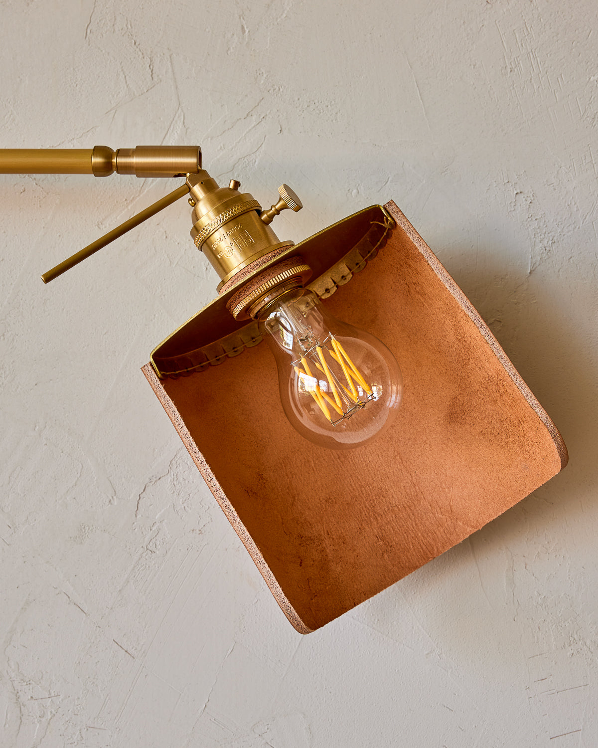 Curved tan leather and brass shade for articulating wall sconce