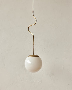 Modern brass globe pendant light with warm satin brass curved body and white milk glass globe