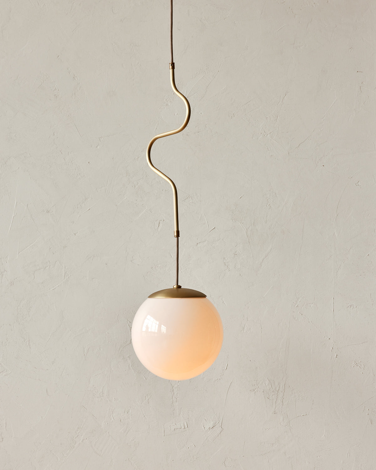 Modern brass globe pendant light with warm satin brass curved body and white milk glass globe