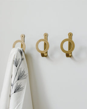 Three oversized brass wall hooks in a line. One holds a white towel patterned with black flowers.